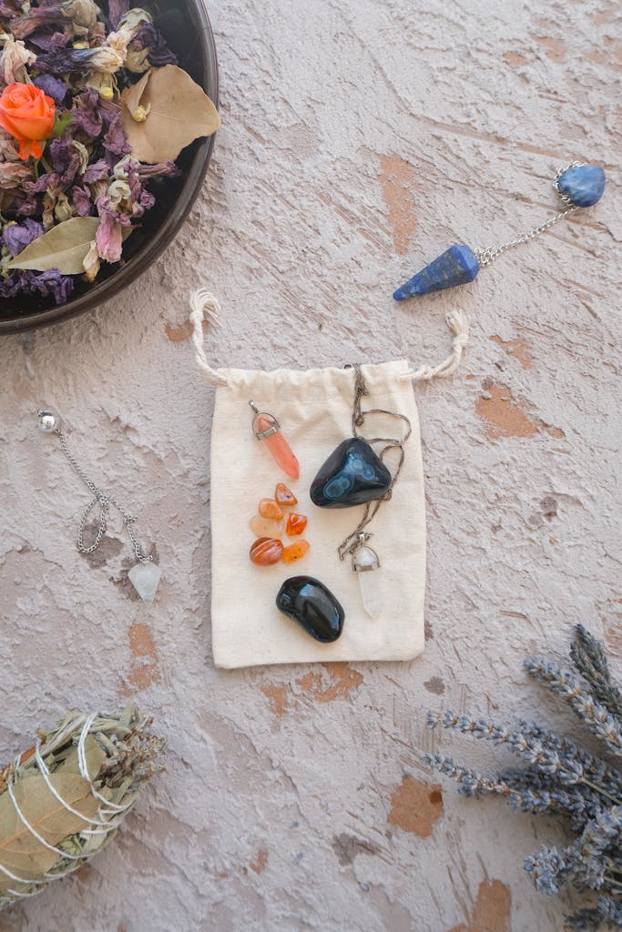 Flat lay of healing crystals, dried flowers, and pendulums for spiritual energy practices.
