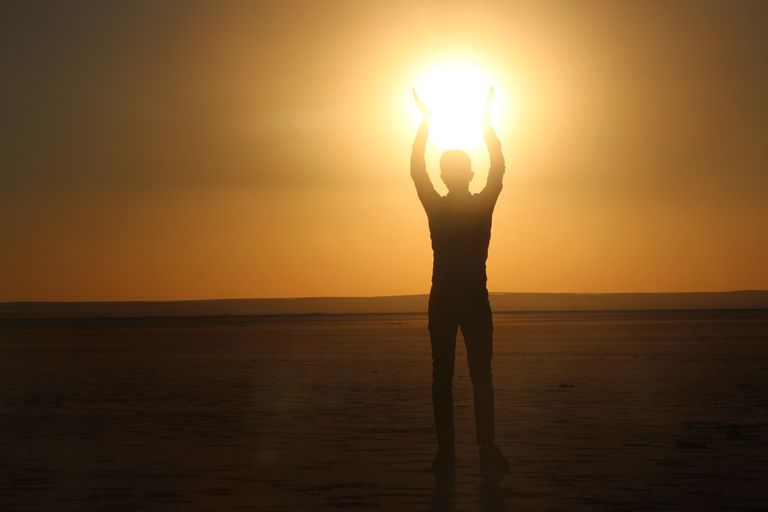 A silhouette of a person raising arms towards the sun during a vibrant sunset, creating a striking visual.