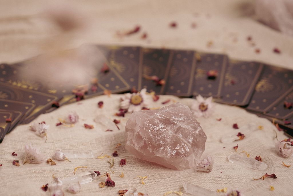 Close-up of rose quartz and tarot cards on fabric, surrounded by dried flowers.